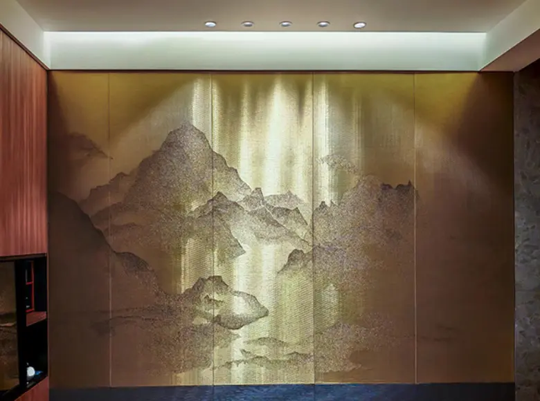 Illuminated Gold-Toned Wire Wall Panel Featuring A Woven Mountain And River Landscape Design In A Modern Interior Setting.